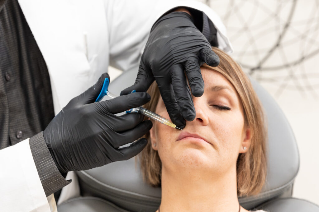 A woman at Enrichment Skin Solutions laying back in a comfortable treatment chair while an experienced injector places filler in her lips, augmenting her natural beauty.
