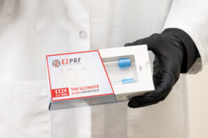 Enrichment Skin Solutions co-founder, Michael Johnson, wearing a white lab coat and black gloves, holds a box of ezPRF vials. This PRF injection is our preference over PRP hair therapy near Plymouth.